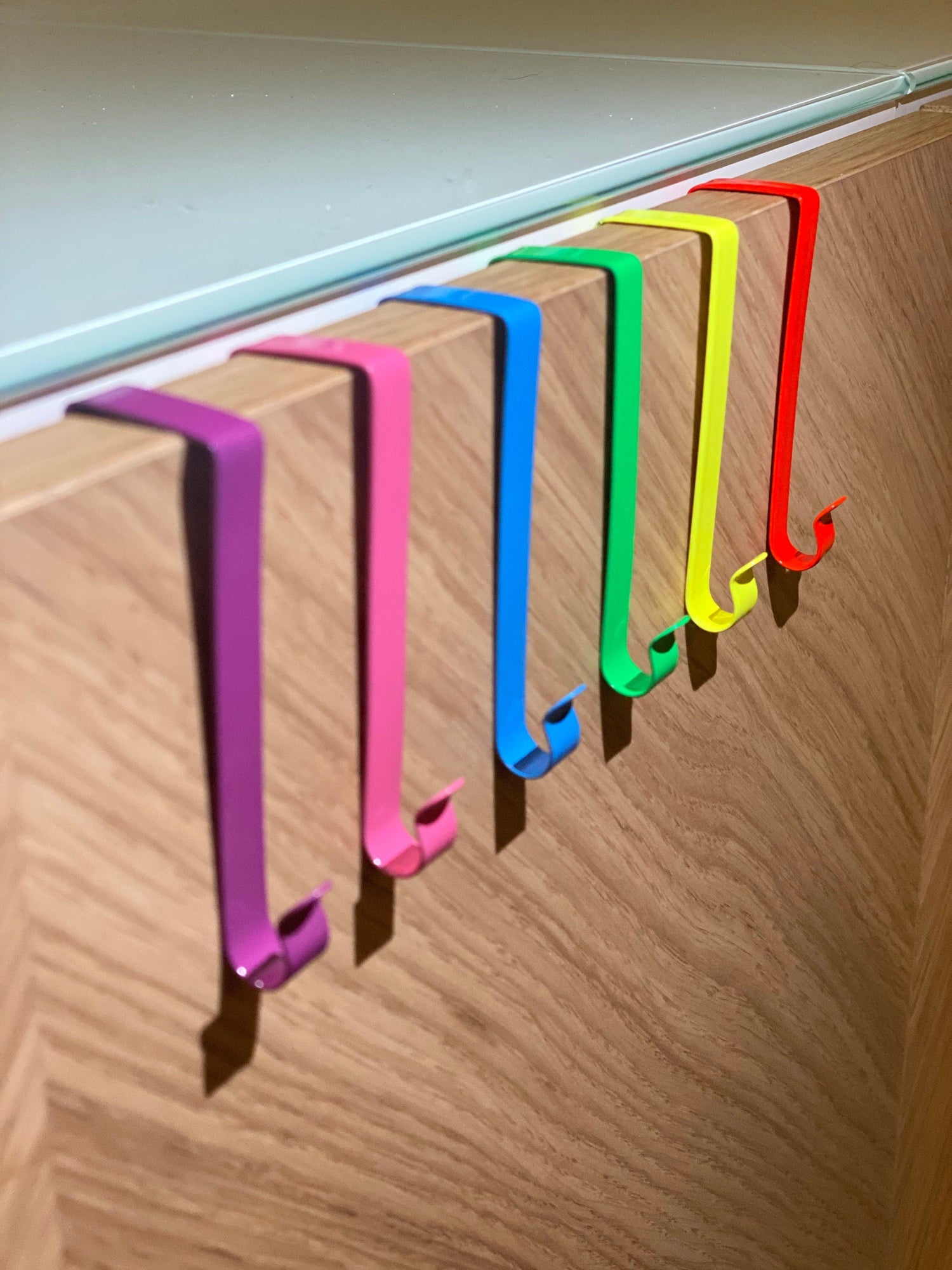 6 Fensterhaken in Regenbogenfarben sind an einer Schranktür befestigt. 